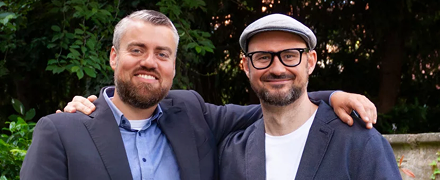 Oskar Hallier und Andreas Rudischhauser, Arm in Arm und lächelnd vor einer Mauer