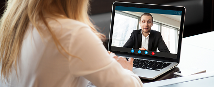 Eine Frau sitzt am Laptop, auf dem Bildschrim läuft ein Videoanruf mit einem Mann als Gegenüber
