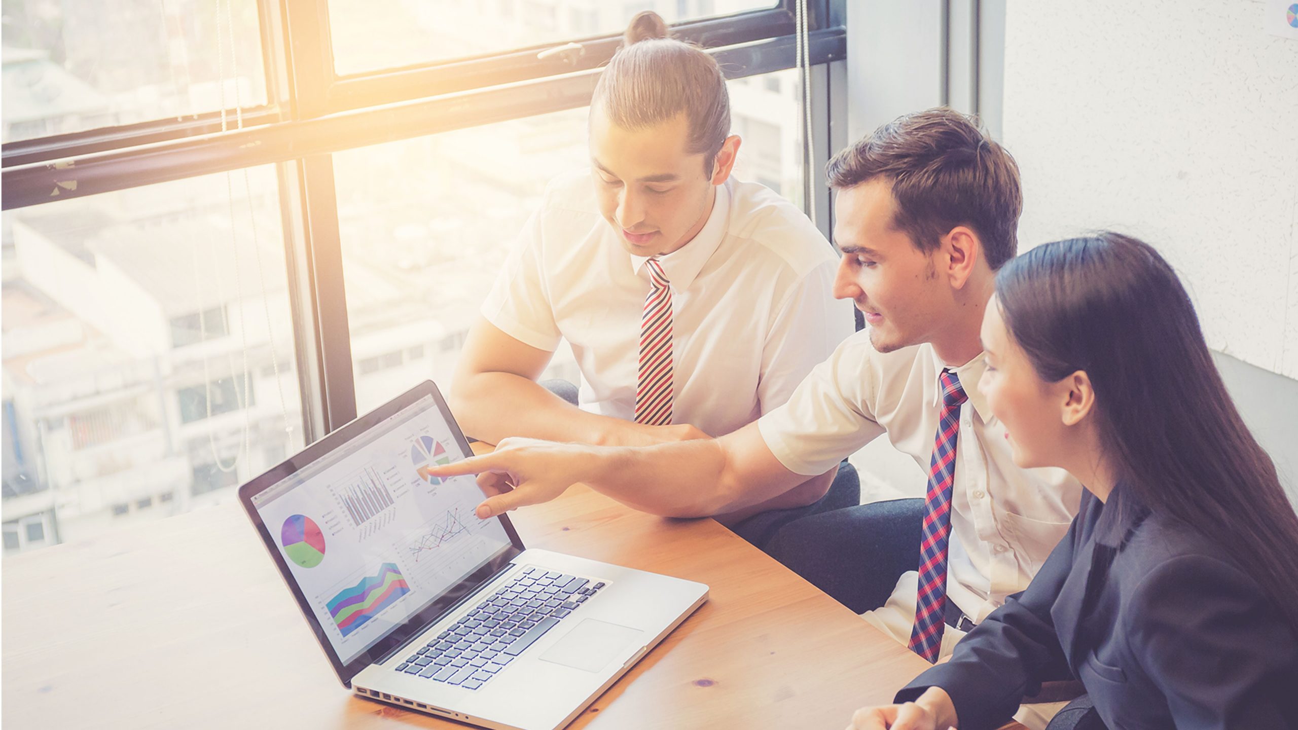3 Personen schauen auf Laptop mit Charts