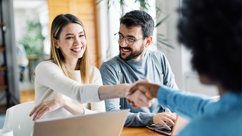 Mann & Frau lächelnd gegenüber weiterer Frau. Frauen schütteln sich die Hände